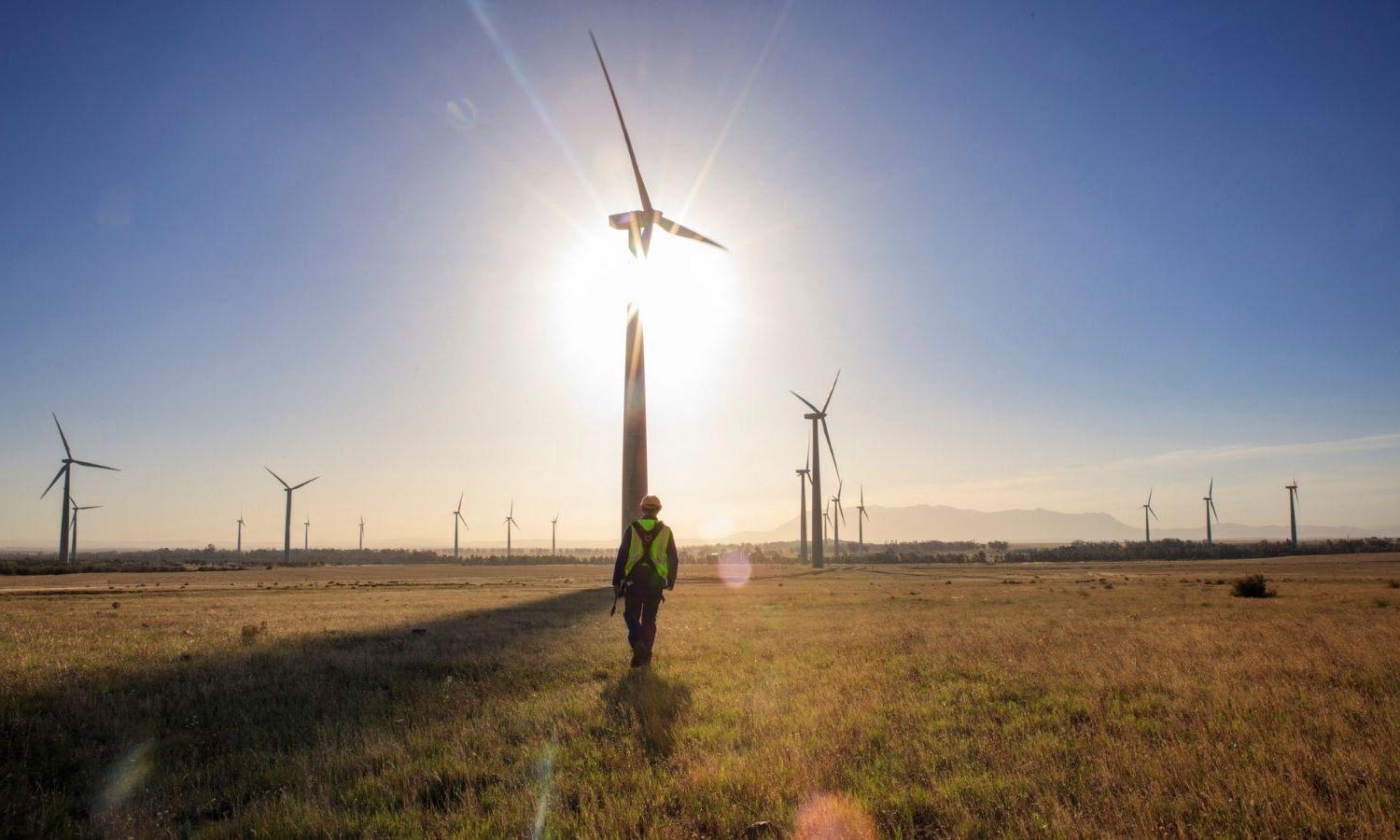 Worker walks toward a wind turbine at sunset.